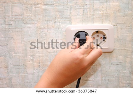 female hand sticks a plug in the socket