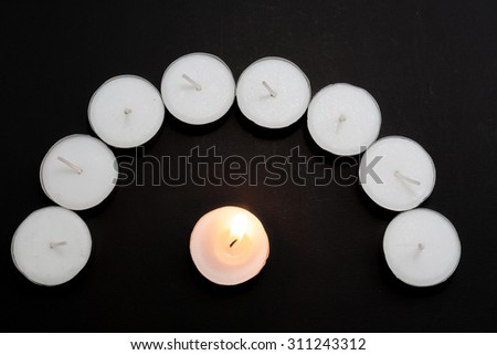 Tea lights candles arranged in arc with one candle being lit on black background