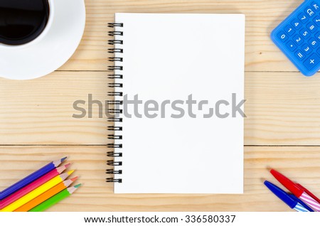Blank notebook with colour-pencils, calculator, pens and  cup of coffee on wooden table