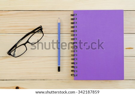 Purple Notebook with pencil and glasses on wooden table