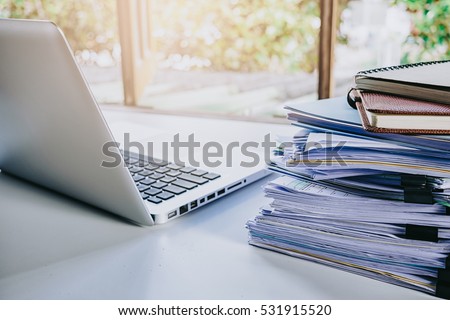 Stack of business report paper file on modern white office desk with laptop computer.Close up business analysis and strategy concept.