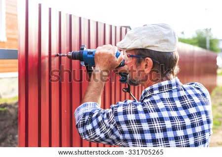 build a metal fence. an elderly man with a drill builds metal fence