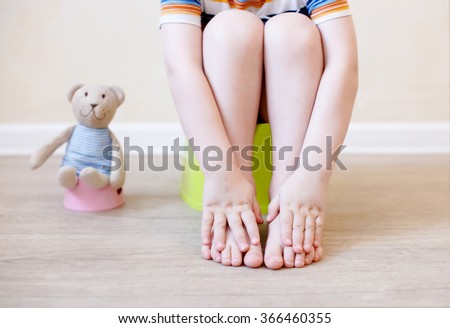 closeup of legs of the child sitting on the potty. the idea of training the child to the potty with a toy bear, which also sits on a toy potty
