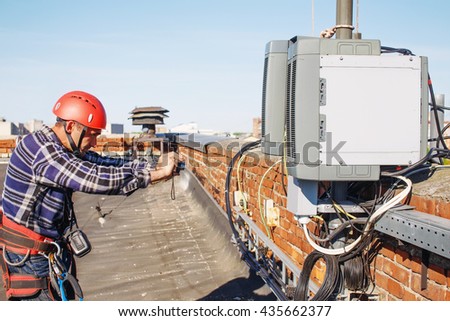 worker finished work and takes photos for the report. quality control. tower technician installed telecommunication equipment on the roof of the building.