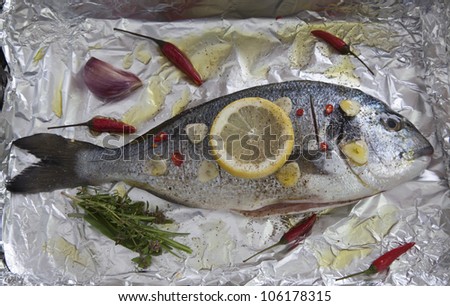 Gilt-head sea bream (sparus aurata) with lemon, herbs, garlic and chili on aluminum foil ready to be cooked