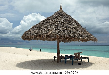 Woman and man relaxing on beach under wooden umbrella. Indian Ocean. Island Zanzibar, Tanzania.