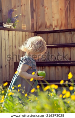 Little girl standing on a country house wooden stairs and holding an apple, natural lighting outdoor shot. Toned photo.