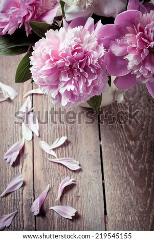 Pink peonies with fallen petals on wooden table, closeup shot. Vintage style toned photo.