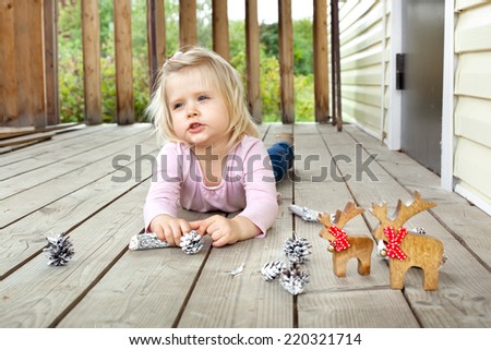 Little girl dreaming of Christmas and presents in summer while playing with Christmas decorations on a country house porch. Natural outdoor lighting setting.