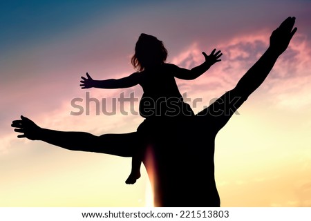 Silhouettes of father and daughter on his shoulders with hands up having fun, against sunset sky