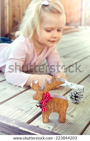 Happy little girl playing with Christmas decorations - reindeer and cones. Natural lighting setting.