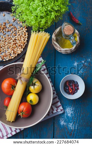 Ingredients for cooking italian pasta - olive oil, tomatoes, pine nuts, spice and herbs on old wooden table, mediterranean cuisine recipe