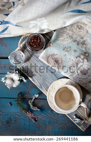 Cup of espresso set on a wooden table with coffee beans, a cup and table linens, natural light setting.