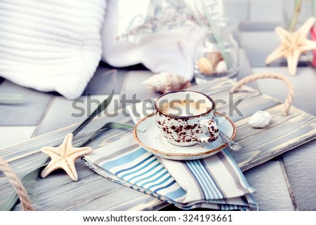 Cup of espresso served on vintage wooden tray, with marine style decorations. Natural light toned photo, with cushions and decorations on the background.