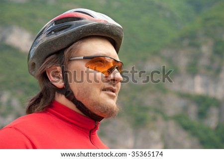 Outdoor portrait of a young cyclist in helmet and sunglasses, observing the mountain scenery