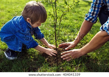 little boy helping his father to plant the tree while working together in the garden. sunday. smiling face.  spring time