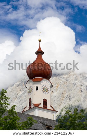 Church tower in front of a mountain and blue sky with white clouds, Austrian Alps, Europe
