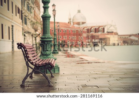 long time exposure of typical wooden bench on promenade in Venice (Venezia) on a rainy day in autumn without people, Italy, Europe, vintage filtered style