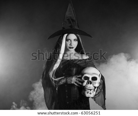 Halloween witch with a skull over black background with smoke. Black and white