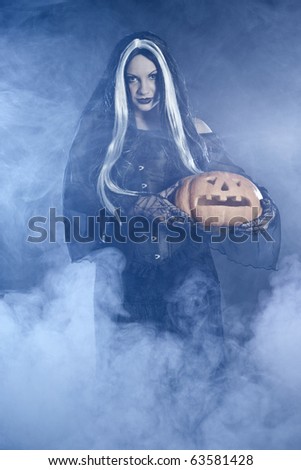 Portrait Halloween witch with a pumpkin. Smoke background