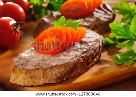Liver pate with cherry tomatoes and herbs on a wooden chopping board