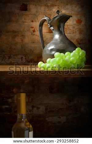Still life of an old metal jug and a bunch of grapes on a shelf, a bottle of wine underneath the wooden shelf, with a worn brick background
