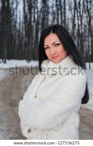 Young brunette woman in white fur coat in winter forest