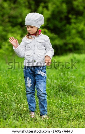 Young girl standing on a green lawn and flapping mosquitoes away