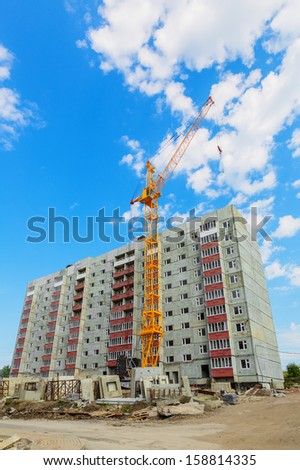 Dwelling house and tower crane on the construction site beneath blue cloudy sky