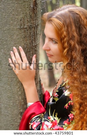 A beautiful ginger-haired girl in gypsy suit near a tree