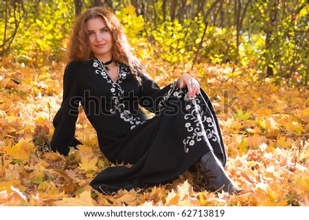 A beautiful ginger-haired woman sitting on the ground in fall forest