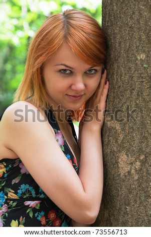 Portrait of a beautiful ginger-haired woman standing near a tree