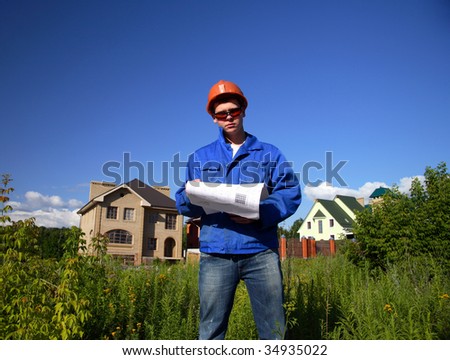 Young man with the plan of construction, background grass and unfinished building houses