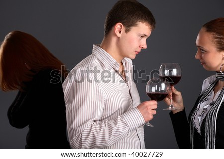 Young couple holding glasses with wine and woman looking at them, studio, gray background