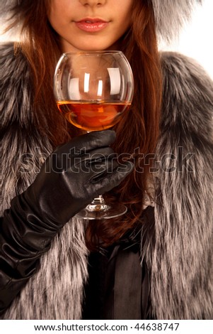 The girl dressed in a fur coat keeps in a hand a glass with an alcoholic drink