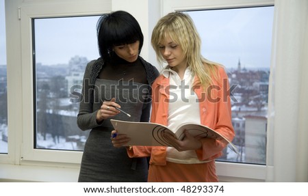 Two businesswomen looking into papers, standing near the window in office