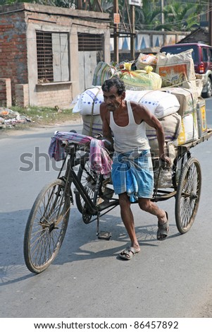 BARUIPUR, INDIA - JANUARY 13: Man pushing heavily loaded cycle rickshaw. The cheaper and simplest public transportation which give poor people work, Baruipur, West Bengal, India on January 13, 2009