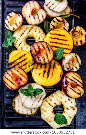GRILLED FRUITS. Grill fruits - pineapple, peaches, plums, avocado, pear on black cast iron grill board.
