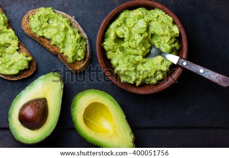 Traditional latinamerican mexican sauce guacamole in clay bowl, cut half avocado and avocado sandwiches on dark background. Top view