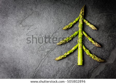 Christmas Food background. Christmas tree made from fresh asparagus on black stone slate background. Healthy holiday food, vegan, vegetarian and diet concept