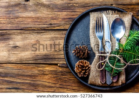 Vintage rustic cutlery set with country style napkin and Christmas decoration - fir tree brunch, cones on black iron plate on wooden background. Copy space, top view. Christmas menu background