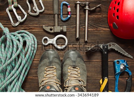 climbing equipment: blue rope, red helmet, hammer, trekking shoes and other set  on dark wooden background, top view