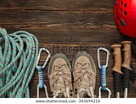 climbing and hiking equipment: blue rope, red helmet, grey shoes and other set  on dark wooden background, top view