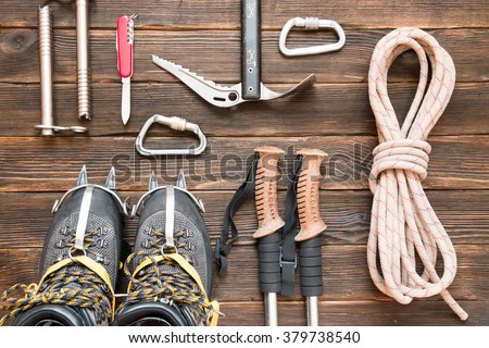climbing equipment: rope, trekking shoes, crampons, ice tools, ice ax, ice screws, red knife and other set on dark wooden background, top view. Travel concept.