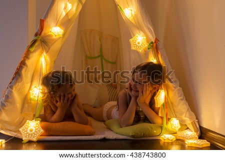 The night. Two little sisters indulge in the tent. Houses, before going to bed, bedside lamp