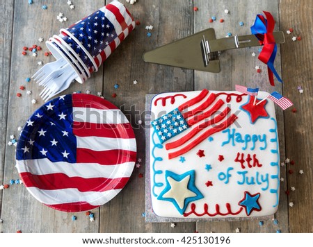 4th of July cake with picnic plates and cups on wooden table, seen from above