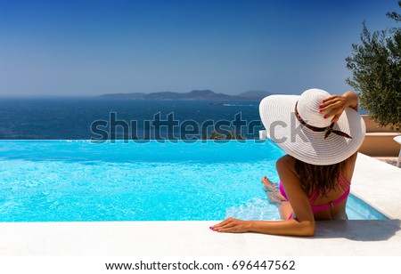 Attractive woman in bikini and with white hat is relaxing in an infinity pool