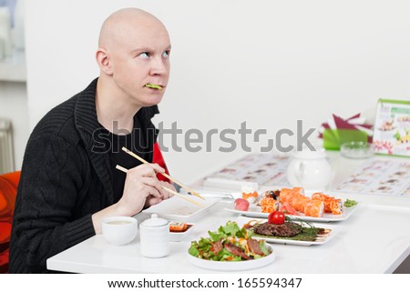 Man with surprised face eats sushi in cafe