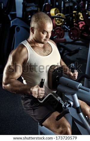Sportive man doing exercise with pull-down machine in the gym