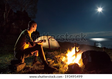 Hiking tourist have a rest in his camp at night near campfire